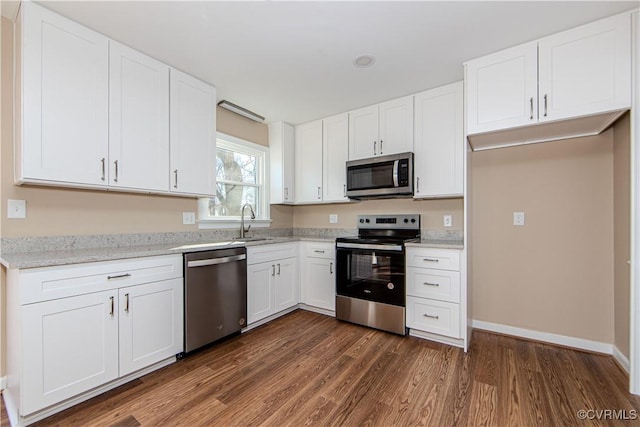 kitchen featuring stainless steel appliances, sink, white cabinetry, light stone counters, and dark hardwood / wood-style flooring