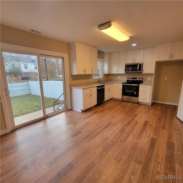 kitchen with stainless steel appliances, sink, white cabinets, and light wood-type flooring