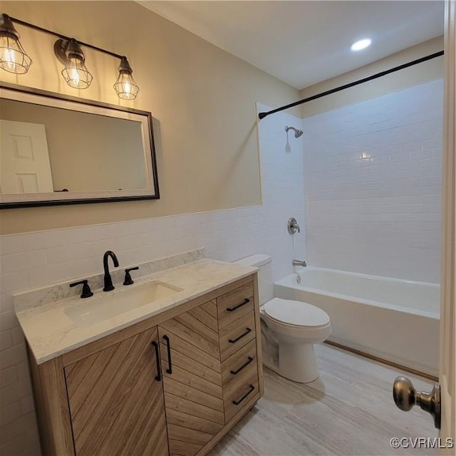 full bathroom with tile walls, vanity, tiled shower / bath combo, and toilet