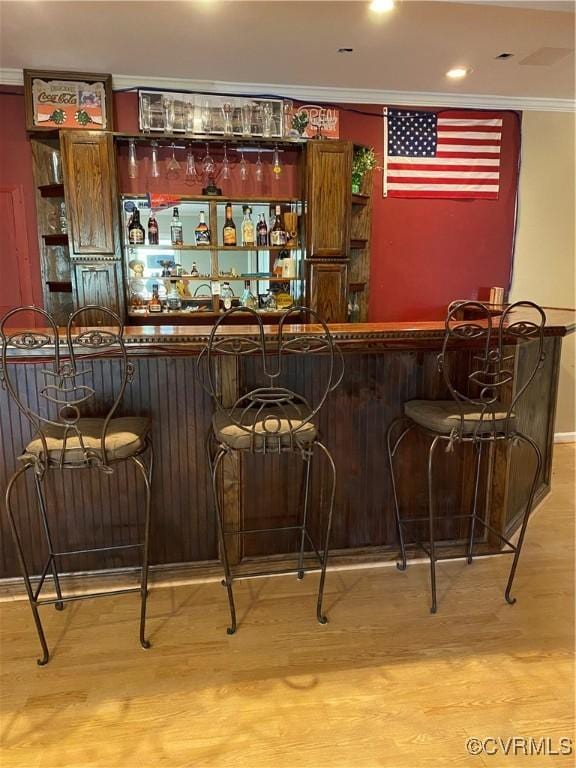 bar with ornamental molding and light hardwood / wood-style floors