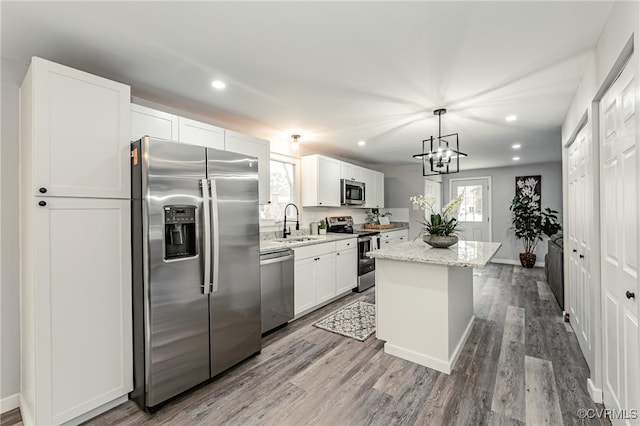 kitchen with pendant lighting, appliances with stainless steel finishes, a kitchen island, white cabinetry, and light stone counters