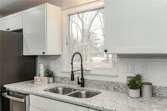 kitchen with decorative backsplash, stainless steel dishwasher, white cabinets, light stone counters, and sink