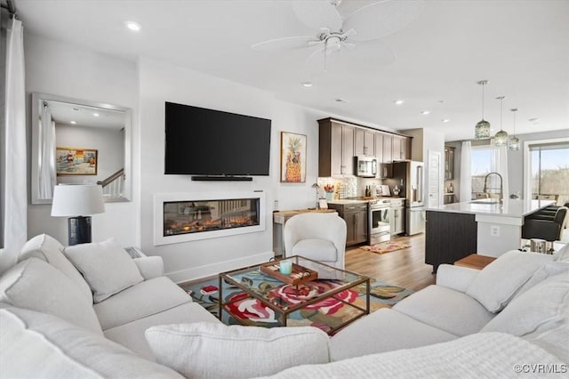 living room featuring ceiling fan, sink, and light wood-type flooring