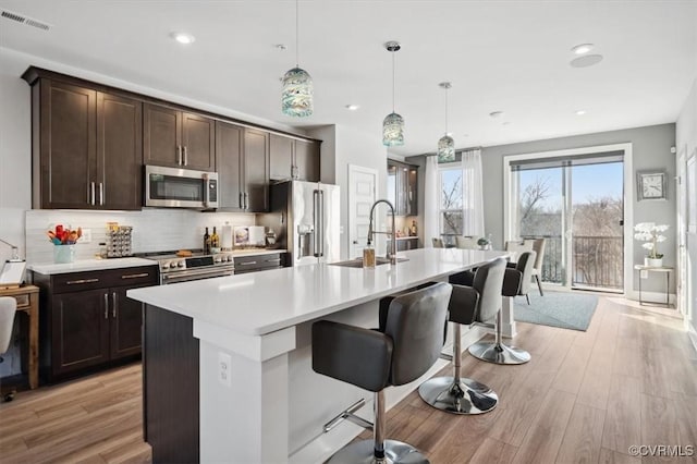 kitchen with pendant lighting, a breakfast bar area, stainless steel appliances, tasteful backsplash, and a center island with sink