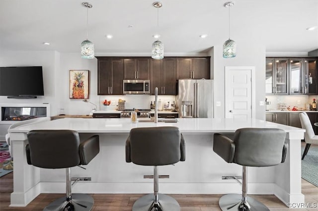 kitchen with dark brown cabinetry, stainless steel appliances, decorative light fixtures, and a breakfast bar area