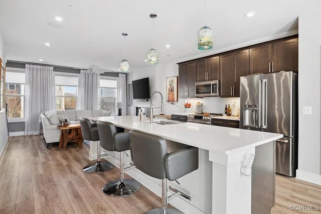 kitchen with sink, dark brown cabinets, appliances with stainless steel finishes, an island with sink, and pendant lighting