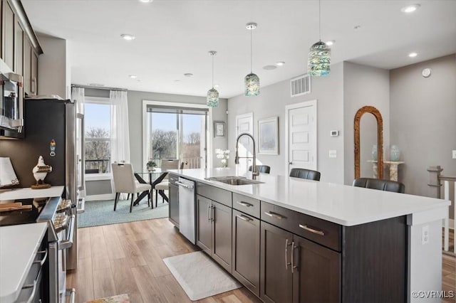 kitchen featuring stainless steel appliances, sink, a center island with sink, and light hardwood / wood-style flooring