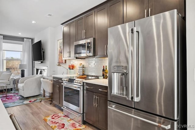 kitchen featuring tasteful backsplash, stainless steel appliances, light hardwood / wood-style floors, and dark brown cabinets