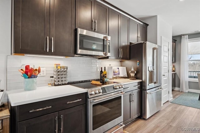 kitchen with tasteful backsplash, dark brown cabinets, stainless steel appliances, and light wood-type flooring