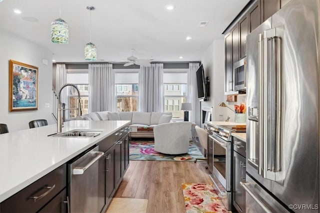 kitchen with dark brown cabinetry, sink, light wood-type flooring, appliances with stainless steel finishes, and pendant lighting