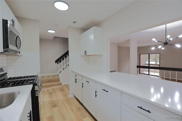 kitchen with appliances with stainless steel finishes, white cabinetry, tasteful backsplash, hanging light fixtures, and a notable chandelier