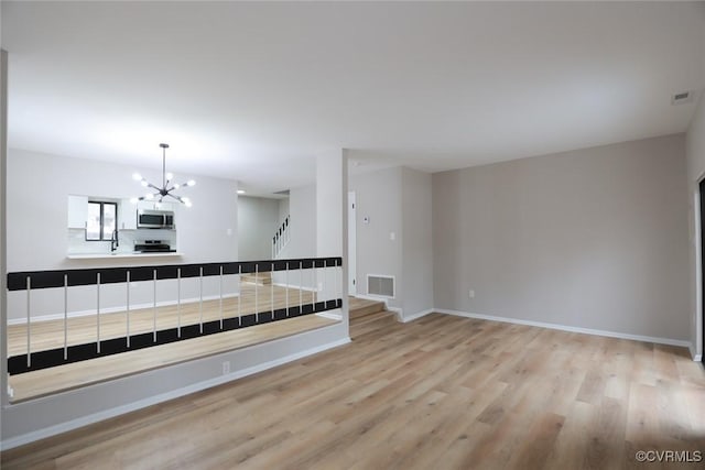 empty room with light wood-type flooring, a chandelier, and sink