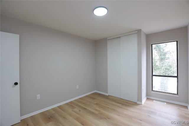 unfurnished bedroom with light hardwood / wood-style floors, multiple windows, and a closet