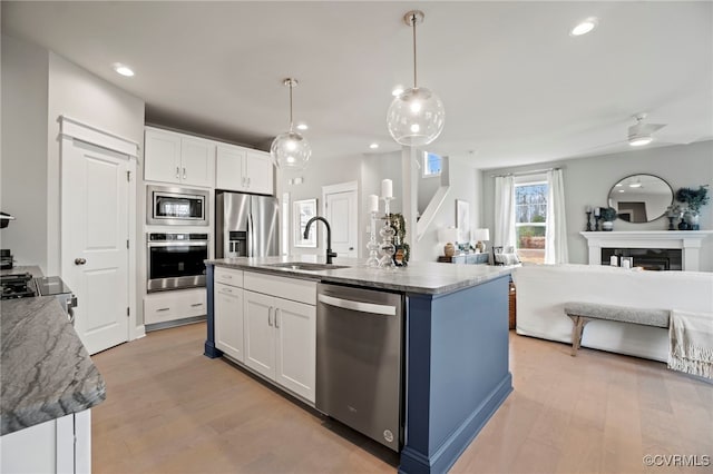 kitchen with appliances with stainless steel finishes, sink, white cabinetry, and a kitchen island with sink