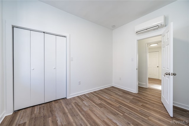 unfurnished bedroom featuring wood-type flooring, a closet, and a wall mounted air conditioner