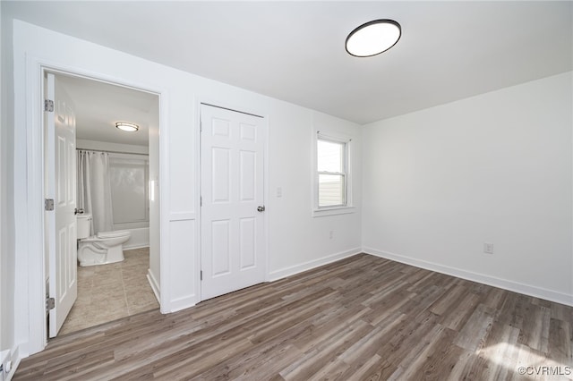 unfurnished bedroom featuring ensuite bathroom, a closet, and hardwood / wood-style flooring