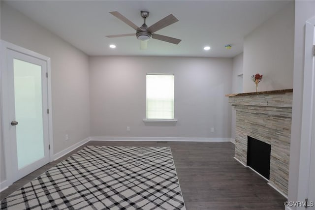 unfurnished living room featuring dark wood-type flooring, ceiling fan, and a stone fireplace