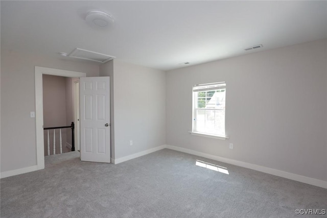 unfurnished room featuring baseboards, visible vents, attic access, and light colored carpet