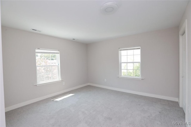 spare room featuring light colored carpet, visible vents, and baseboards