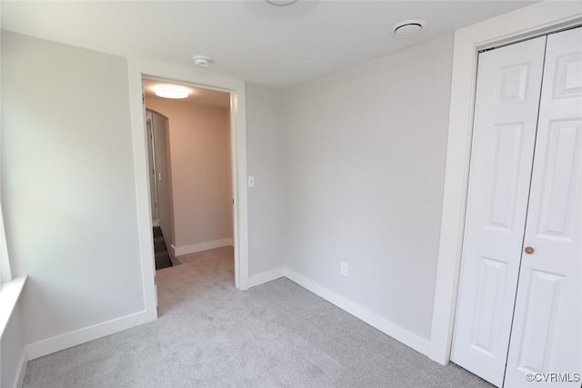 unfurnished bedroom featuring light carpet, baseboards, and a closet