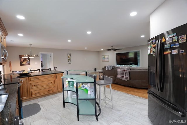 kitchen with black refrigerator with ice dispenser, ceiling fan with notable chandelier, hanging light fixtures, and a kitchen breakfast bar