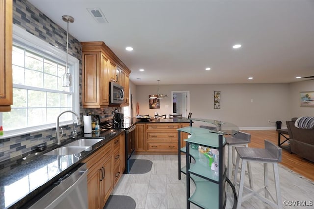 kitchen with a kitchen bar, kitchen peninsula, appliances with stainless steel finishes, decorative light fixtures, and sink