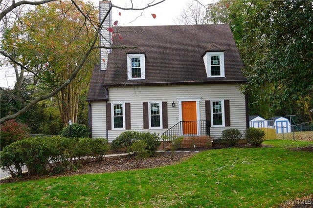 cape cod-style house featuring a front lawn and a storage shed