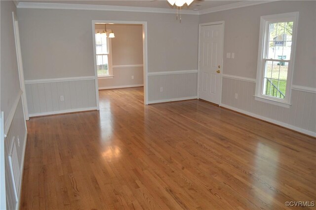 empty room featuring ceiling fan with notable chandelier, hardwood / wood-style floors, and crown molding