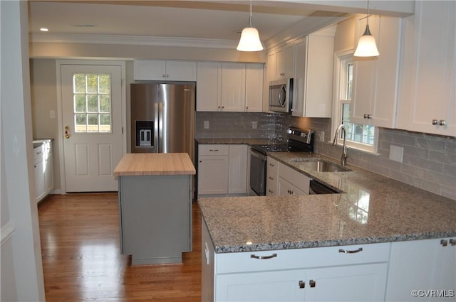 kitchen featuring appliances with stainless steel finishes, a kitchen island, white cabinetry, sink, and hanging light fixtures