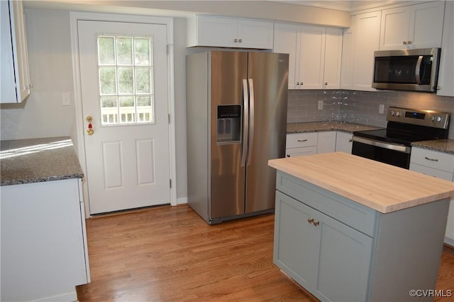 kitchen featuring white cabinetry, stainless steel appliances, backsplash, dark stone counters, and a kitchen island