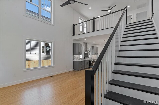 stairs with ceiling fan, wood-type flooring, and a high ceiling