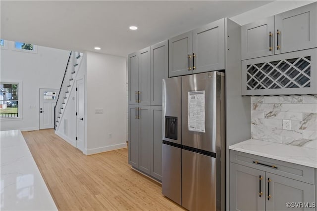 kitchen featuring light wood-type flooring, light stone counters, stainless steel fridge with ice dispenser, and gray cabinetry