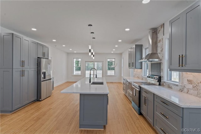 kitchen featuring pendant lighting, appliances with stainless steel finishes, wall chimney range hood, gray cabinets, and a center island with sink