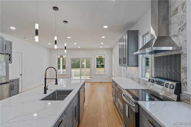 kitchen featuring light stone countertops, wall chimney exhaust hood, stainless steel appliances, sink, and hanging light fixtures