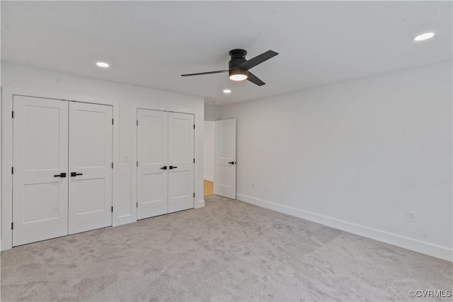 unfurnished bedroom featuring ceiling fan, multiple closets, and light carpet