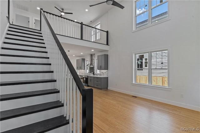 stairs with ceiling fan, wood-type flooring, and a towering ceiling