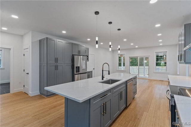 kitchen with light stone countertops, appliances with stainless steel finishes, sink, gray cabinets, and a center island with sink