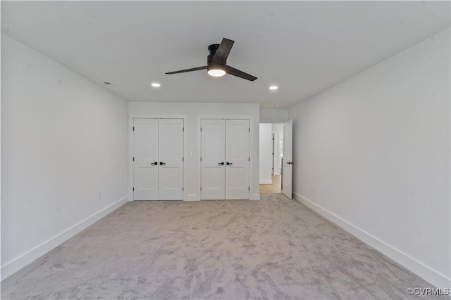 unfurnished bedroom with ceiling fan, light colored carpet, and multiple closets