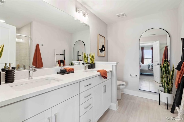 ensuite bathroom with double vanity, a stall shower, connected bathroom, toilet, and a sink