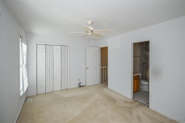 unfurnished bedroom featuring a closet, ensuite bathroom, light colored carpet, and ceiling fan