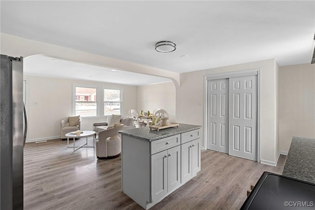 kitchen with light wood-type flooring, dark stone counters, and stainless steel refrigerator