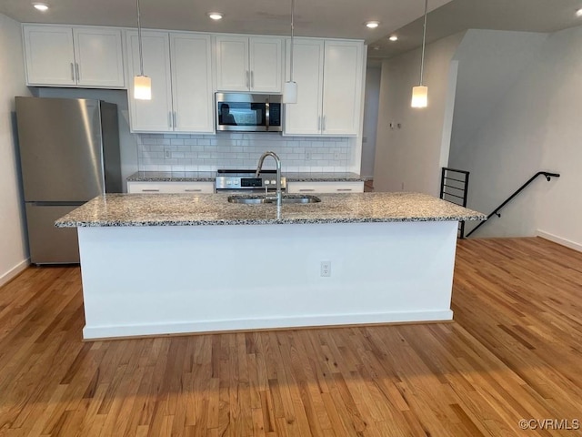 kitchen featuring light stone countertops, white cabinetry, stainless steel appliances, sink, and a kitchen island with sink