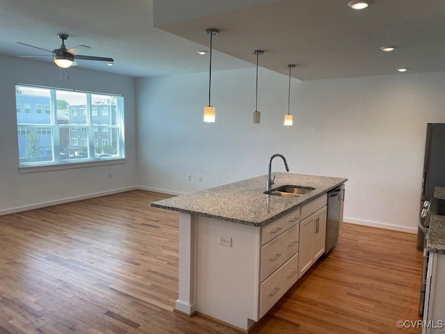 kitchen with sink, hanging light fixtures, light stone countertops, an island with sink, and white cabinets