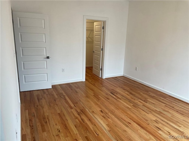 unfurnished bedroom featuring a walk in closet, a closet, and light hardwood / wood-style floors