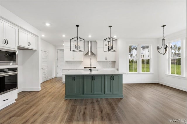 kitchen with white cabinets, appliances with stainless steel finishes, wall chimney range hood, and pendant lighting