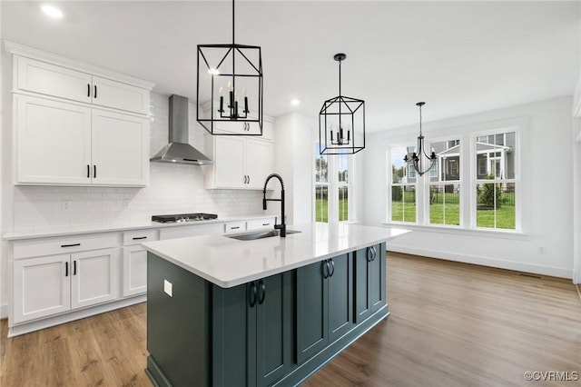 kitchen with white cabinetry, sink, wall chimney range hood, and pendant lighting