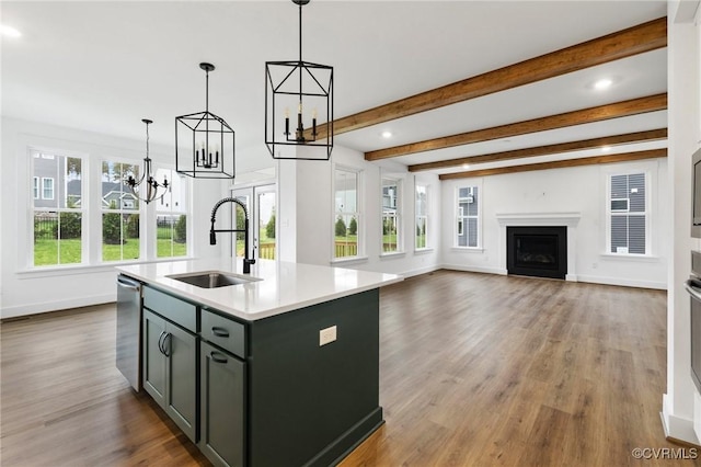 kitchen with pendant lighting, beam ceiling, sink, hardwood / wood-style flooring, and a kitchen island with sink