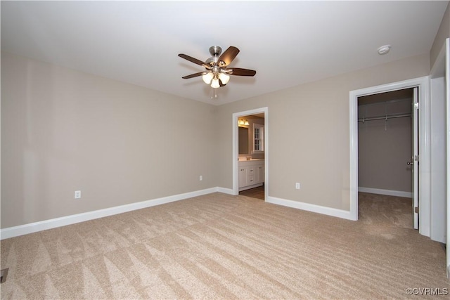 unfurnished bedroom featuring ensuite bathroom, ceiling fan, a closet, light colored carpet, and a walk in closet