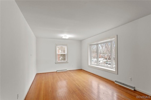 spare room featuring baseboard heating, a wealth of natural light, and light hardwood / wood-style flooring