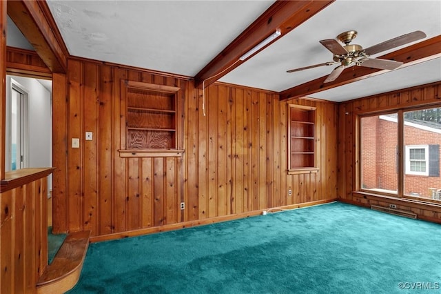 empty room featuring wooden walls, ceiling fan, carpet, built in features, and beam ceiling